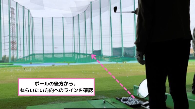 ゴルファーがボールの後方からアライメントを確認している。