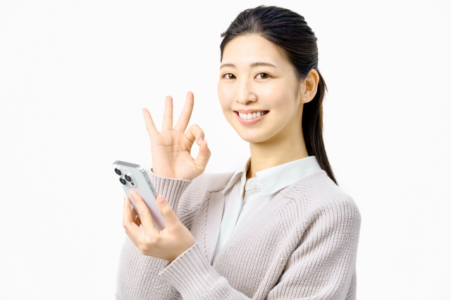 スマホを持ちOKサインをする女性。